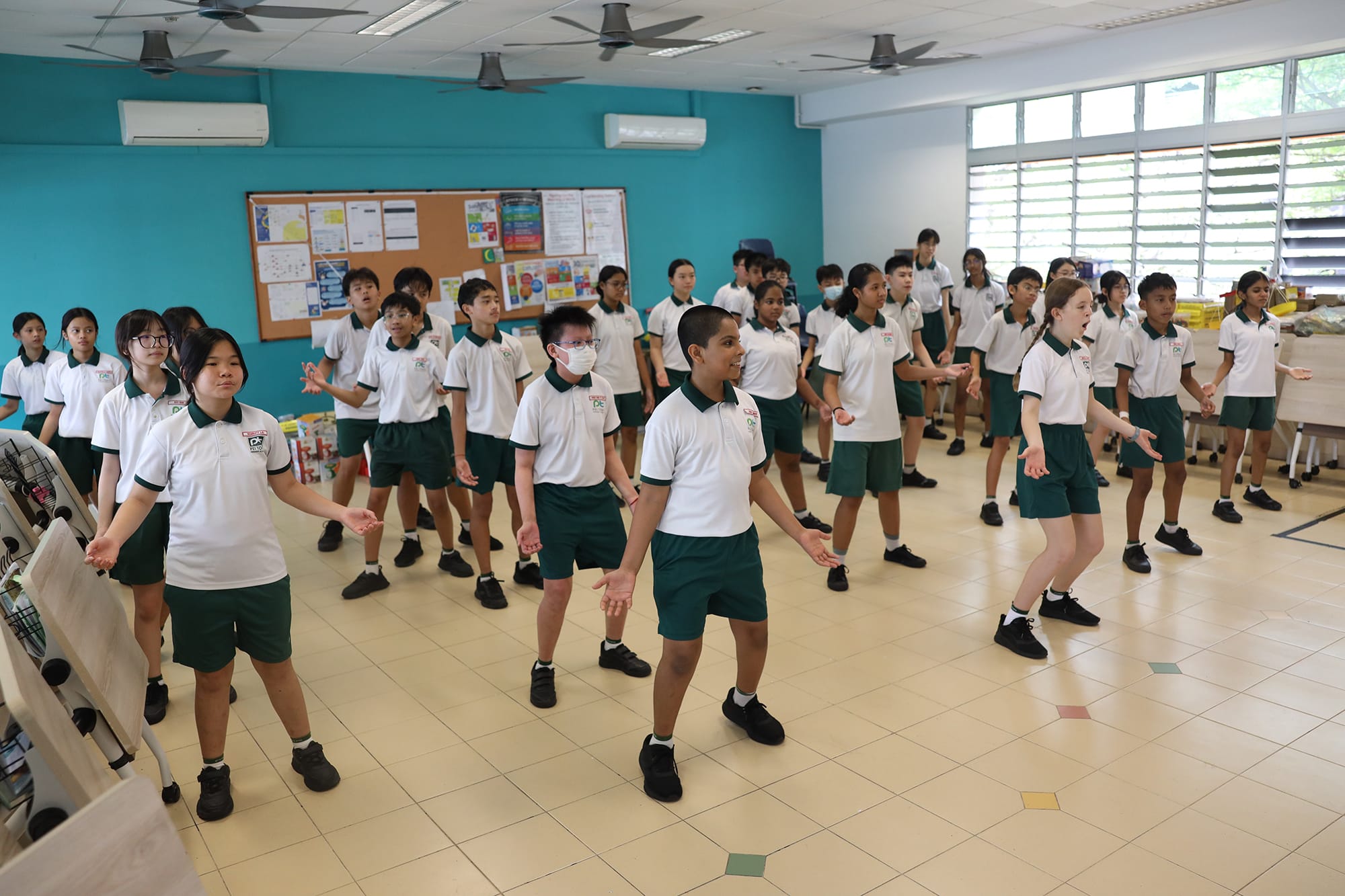 Students stand in rows inside a classroom with their arms positioned for a dance routine as they follow the instructor during a Hip Hop dance lesson.